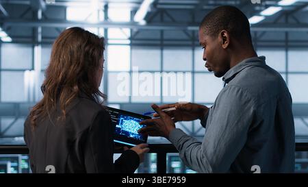 Data center system administrators using artificial intelligence neural networks tech on tablet. Teamworking server farm employees using AI programming language on device screen, camera A Stock Photo
