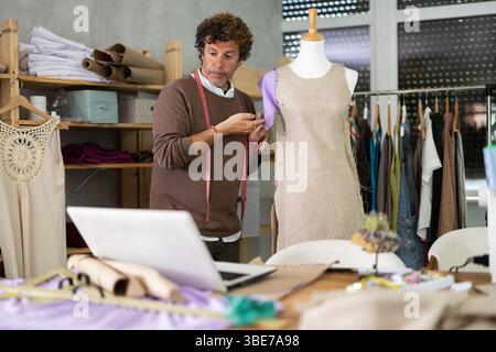 Man seamstress communicates with customer via video call using laptop, work with mannequin Stock Photo