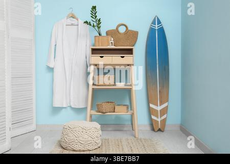 Interior of stylish room with table, folding screen, bathrobe and surfboard Stock Photo