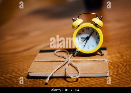 A bright yellow alarm clock and notebook with string create a cozy, charming scene on a wooden desk. A simple and cozy scene perfect for study concept Stock Photo