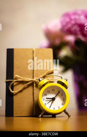 Beautiful pink peonies in a purple vase with a vintage alarm clock and a notebook. A delicate bouquet of pink spring flowers on a wooden table at home Stock Photo