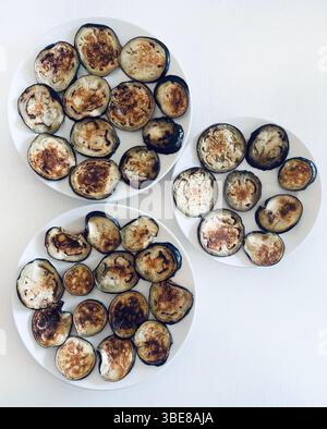 Grilled aubergine slices in a white plates isolated on a white table. Healthy and vegetarian food.  Directly above. Stock Photo