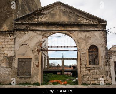 An arched entrance to a derelict building in central Pula, Croatia. It features a classical triangular pediment with two windows flanking the arch Stock Photo