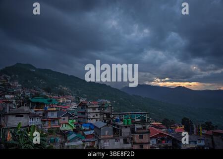 A picturesque small town nestled within lush green hills, photographed at twilight under a captivating partly cloudy sky. Stock Photo