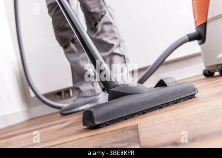 Cleaning a wooden floor with a vacuum cleaner while sunlight pours in from a nearby window, showcasing the tidiness of the space. Stock Photo
