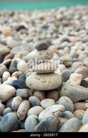 beautiful grey and white pebbles stacked on a beach and turquoise sea in background Stock Photo