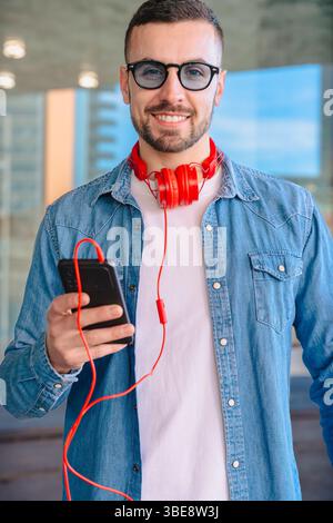 Smiling man using smartphone and holding coffee cup in modern urban setting Stock Photo