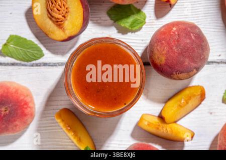 Homemade sweet sour peach chutney jam preserves with spices and raisins, in small jar, with fresh ripe peaches on white wooden table Stock Photo