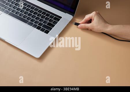 female hand connecting charger cable to laptop at beige table, closeup Stock Photo