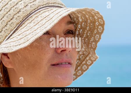 Close up woman face in sun hat looking aside over blue sea Stock Photo