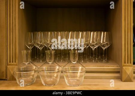 Clean empty wine glasses and decanters are neatly arranged on a wooden shelf, ready for use in a restaurant or bar setting Stock Photo