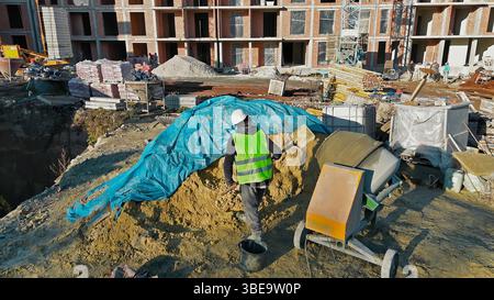Construction worker in safety gear mixing cement on a building site with materials around. Stock Photo