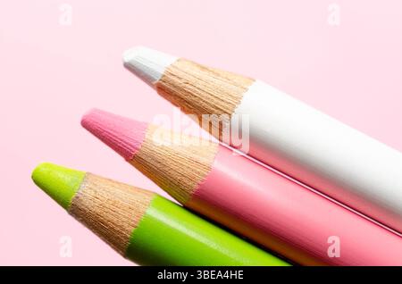 Close-up of three colored pencils in pastel colors on pink background. Stock Photo