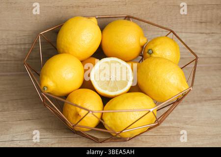 Fresh lemons in metal basket. Citrus fruits on wooden table. Juicy yellow ingredients. Organic vitamin C source. Healthy food concept. Rustic kitchen. Stock Photo