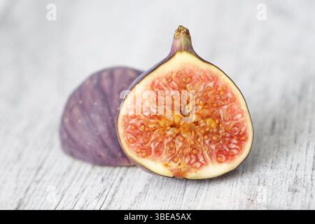 Fresh ripe fig fruit. Halved fig on white table. Organic healthy snack idea. Tropical sweet taste. Natural dessert concept. Juicy exotic fruit closeup. Stock Photo