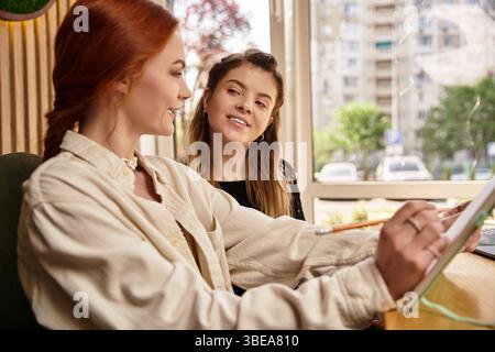 Two young women engage in creative work while enjoying each others company in a cafe. Stock Photo