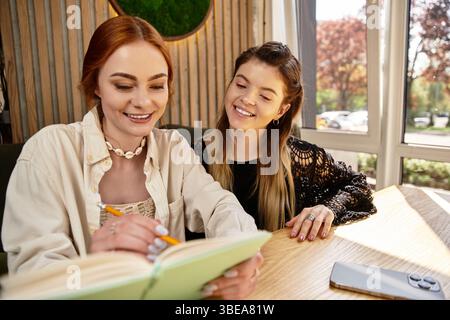 Two young women study together, exchanging ideas in a cozy cafe setting. Stock Photo