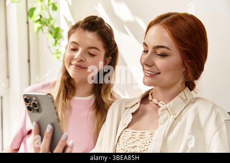 Two beautiful young women share a joyful moment in a stylish cafe while interacting with phone. Stock Photo