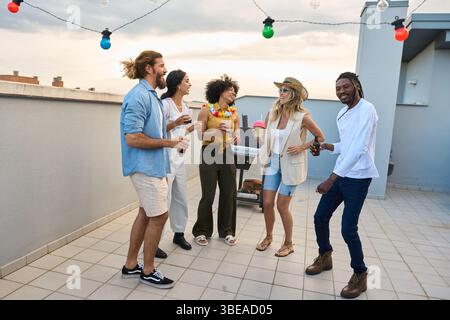 Friends enjoying drinks and dancing at rooftop party Stock Photo