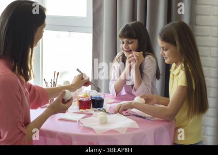 Mother and two daughters at the table paint easter eggs Stock Photo