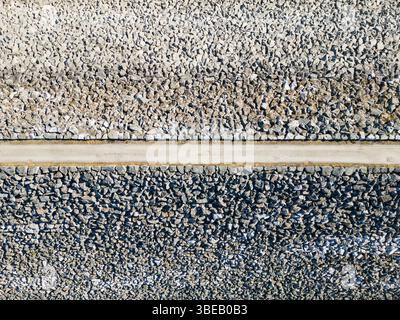 Aerial top-down view of a narrow path dividing contrasting light and dark gravel textures, creating an abstract background. Stock Photo