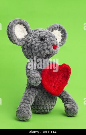 Grey knitted mouse with a heart in hand on a green background, side view Stock Photo