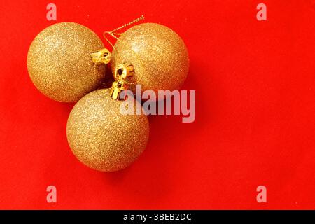 Christmas decoration. Three glittery golden balls. Minimalistic. Close up and isolated with a red background. Copy space for text. Inside aerial view. Stock Photo