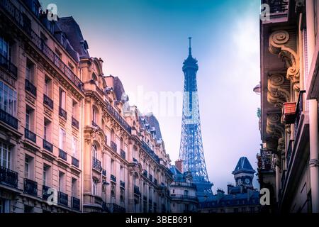 A breathtaking view of the Eiffel Tower peeking above classic Parisian architecture during dusk. Soft lights illuminate the buildings. Paris. France Stock Photo