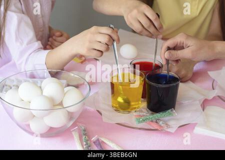 Children interfere with a solution with food coloring in glasses to paint Easter eggs Stock Photo