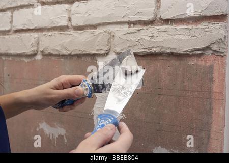 Plasterer works with two spatulas applying plaster on the wall Stock Photo