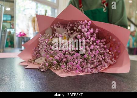 Close-up of a delicate floral bouquet with white orchids and pink baby's breath wrapped in pastel pink paper. Flower shops, gift services Stock Photo