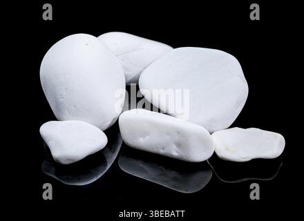 A collection of smooth, matte white pebbles is arranged on a glossy black surface, creating a simple yet elegant composition with subtle reflections, Stock Photo