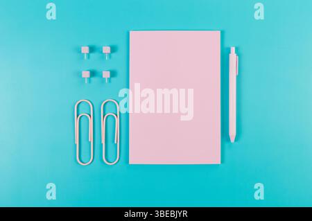 Top view of pink notebook on blue background. Paperclips, pen and pins. School, office wallpaper. Flat lay, copy space. Stock Photo