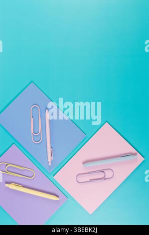 Top view of pink, purple and blue notebooks on blue background. Pink, yellow and blue pens, paperclips, school, office wallpaper. Flat lay, copy space. Stock Photo