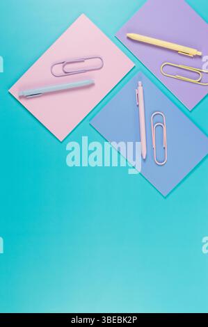 Top view of pink, purple and blue notebooks on blue background. Pink, yellow and blue pens, paperclips, school, office wallpaper. Flat lay, copy space. Stock Photo