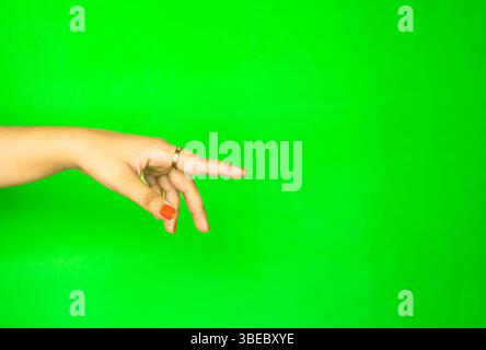 A hand extending forward in a subtle reaching pose on a plain green background. Perfect for product placement in tech, cosmetics, or lifestyle industr Stock Photo