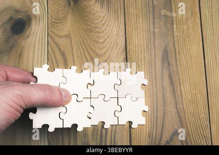 Human hand connecting puzzle pieces on a wooden table. Business concept, union, and business growth. Stock Photo
