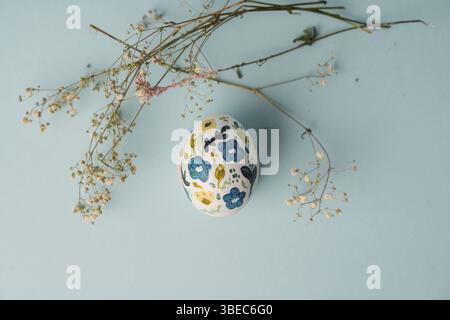 Painted chicken egg in floral pattern. DIY craft for easter holidays with kids. Botanical decoration. Minimal easter egg on blue background. Craft for Stock Photo