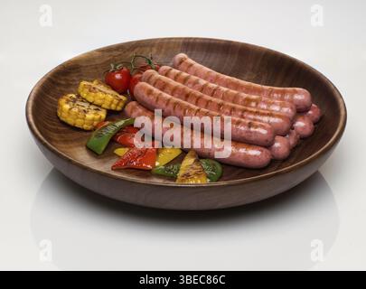 Fried sausages with vegetables in a wooden plate, isolated on a white background Stock Photo