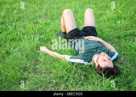 Image of young man with green t-shirt lying on grass in park after exercising exhausted Stock Photo
