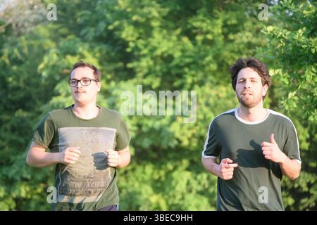 Two masculine friends running with green t-shirt exercising in park on sunny day Stock Photo