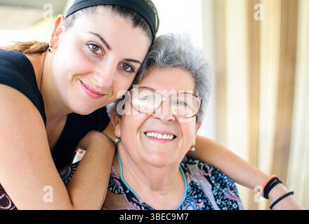 Grandmother with grey hair and glasses smiling with her granddaughter on terrace of her house Stock Photo