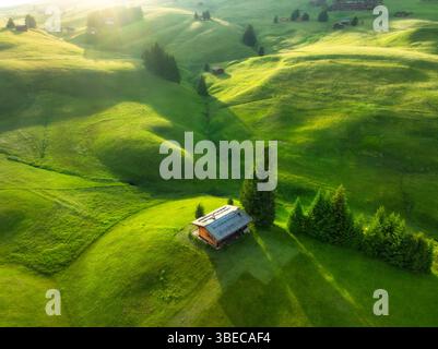 Aerial view of green alpine meadows with houses on the hills at sunset in summer. Top view of mountain valley with trees, green grass and blue sky wit Stock Photo