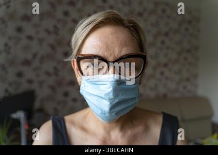 Caucasian woman with medical mask at home. Loneliness, mental health in quarantine. Middle aged mature people. High quality 4k footage Stock Photo