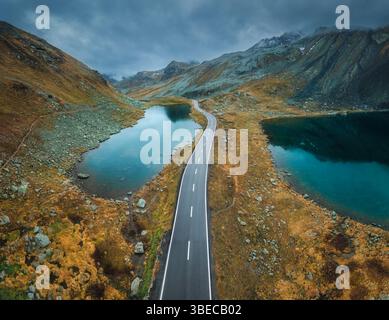 Aerial view of mountain road between two lakes in alpine valley in cloudy autumn day in Switzerland. Top drone view of empty road in swiss mountain pa Stock Photo