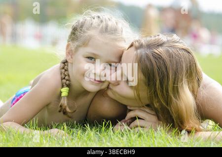 Mother kissing her daughter lying on a green grass lawn Stock Photo