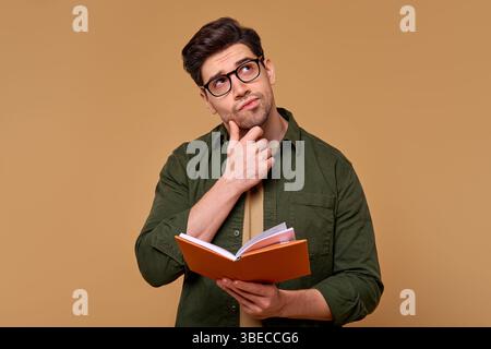 A young man wearing glasses is deeply contemplating while immersed in reading a book, his thoughtful and inquisitive expression illuminated by the war Stock Photo