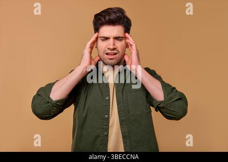 A young man is visibly frustrated and stressed, lifting both hands to his head in a gesture of distress, all against the backdrop of a simple, uniform Stock Photo