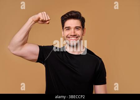 A fit, muscular young man proudly flexes his powerful biceps, showcasing his strength and fitness in a vibrant, uplifting environment that inspires ev Stock Photo