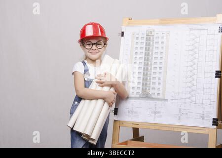 Girl Builder, architect, holding a bunch of drawings, standing at the blackboard with the drawing of the building Stock Photo